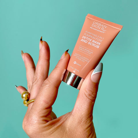 Hand holding a tube of Urban Skin Rx travel size Purifying 2-in-1 Pumpkin Mask and Scrub.