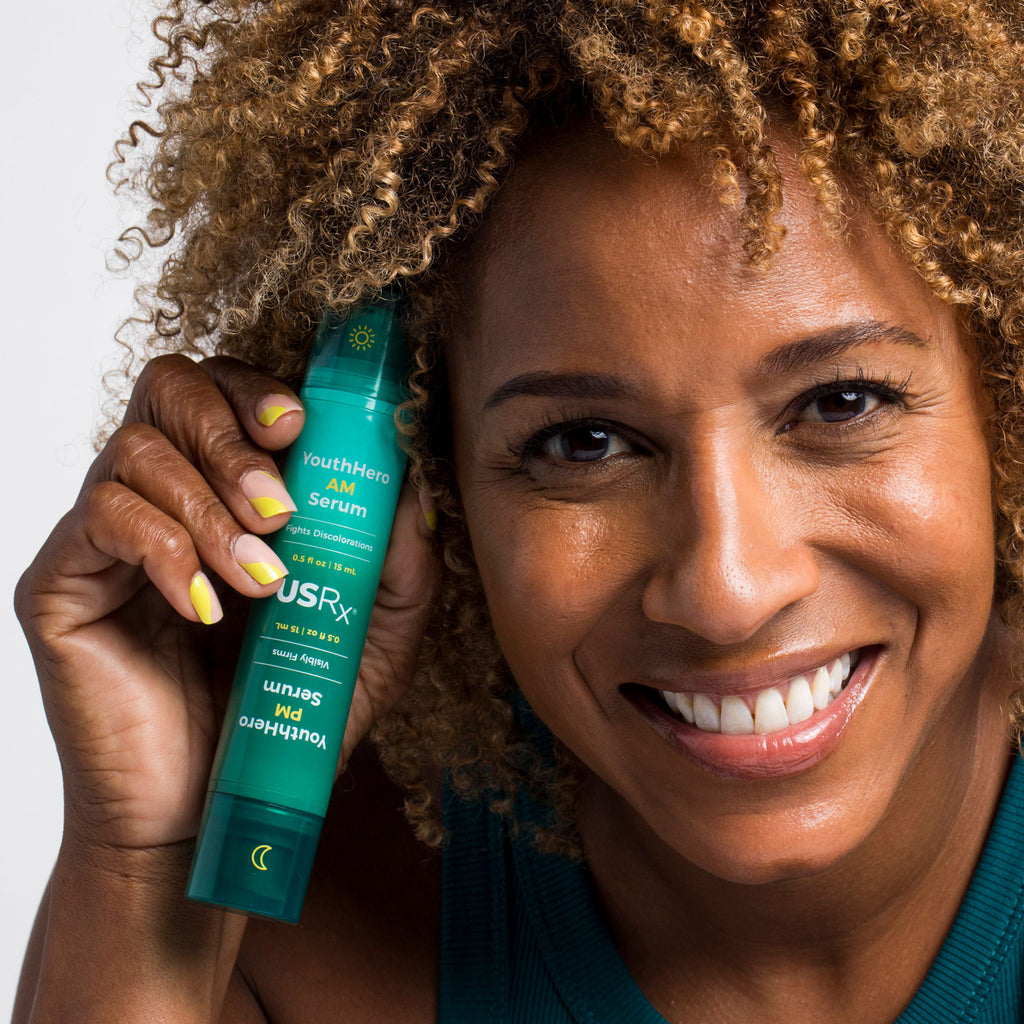 Woman holding bottle of Urban Skin RX YouthHero AM/PM Serum next to her face