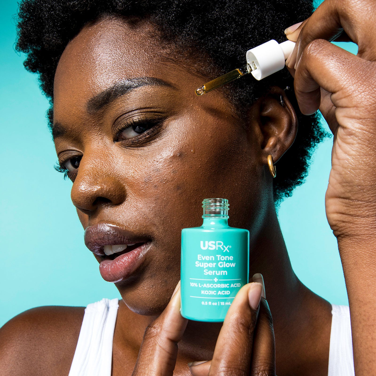 Woman holding bottle of Urban Skin RX Even Tone Super Glow Serum and applying it to her face