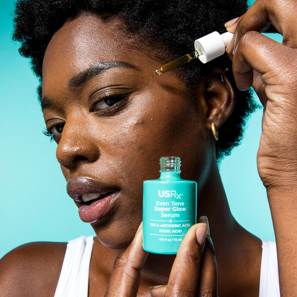 Woman holding bottle of Urban Skin RX Even Tone Super Glow Serum and applying it to her face