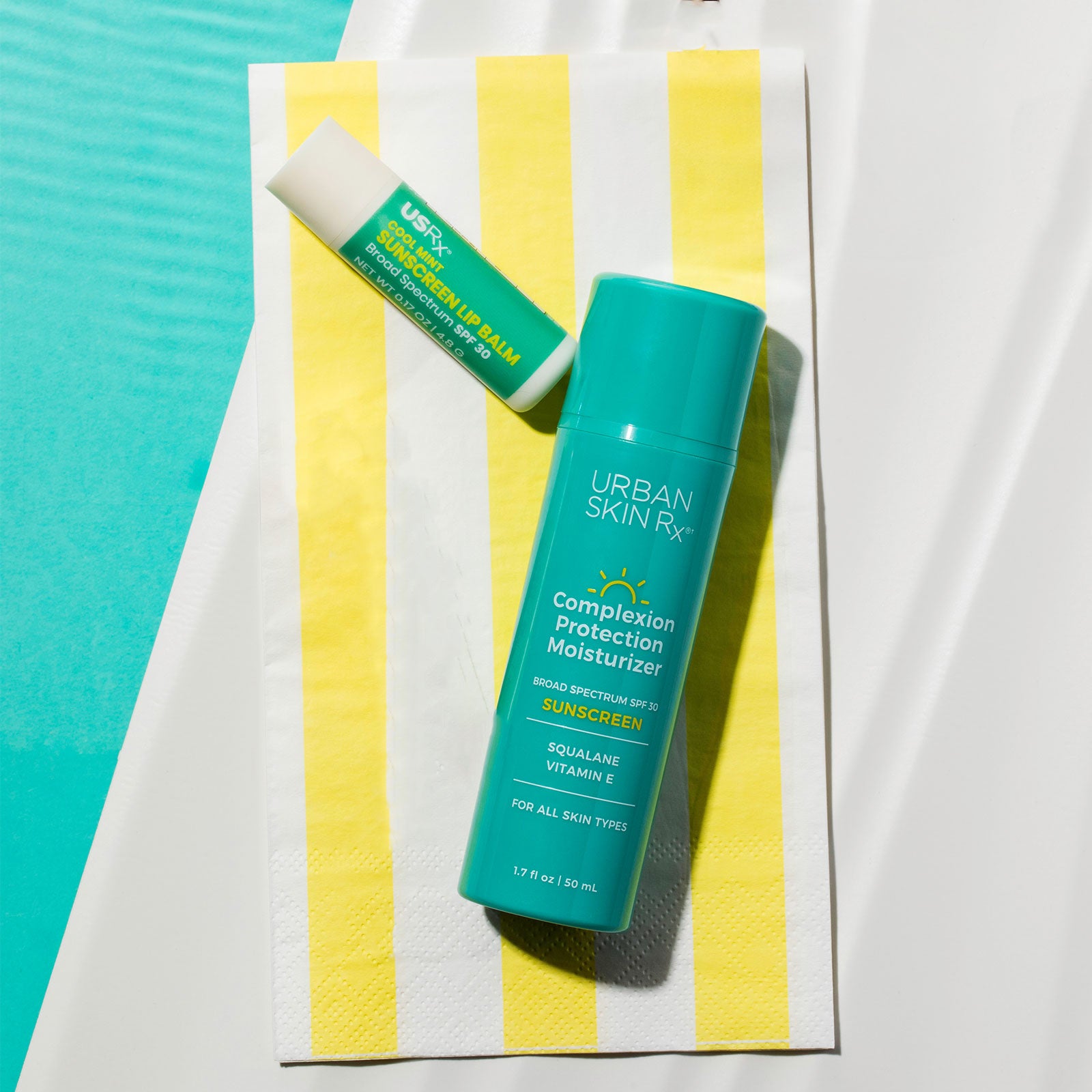 Duo of Urban Skin RX Sunscreen Lip Balm and Complexion Protection Moisturizer Sunscreen SPF30 set against yellow striped beach towel
