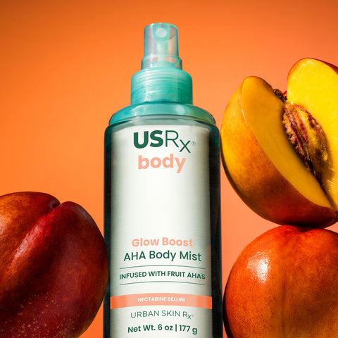 Bottle of USRX Glow Boost AHA Body Mist in Nectarine Bellini next to nectarines
