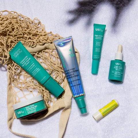 Urban Skin Rx Summer Essentials Bundle featuring six skincare products for a full A.M. and P.M. routine on a textured surface with a net bag.