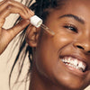 African American model using dropper to apply Reti- Glow Resurfacing Night Oil to her face