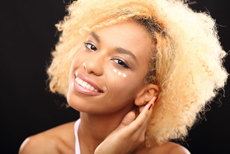 woman smiling and applying under eye cream
